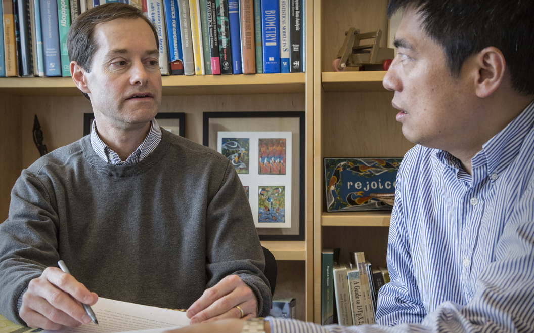 Photo of Peter Gilbert sitting at a table conferring with another researcher