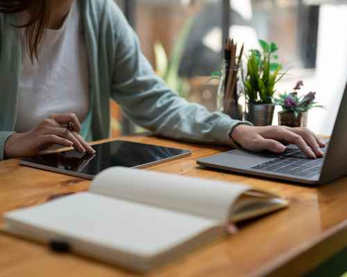 woman working at a desk using a laptop and a tablet 