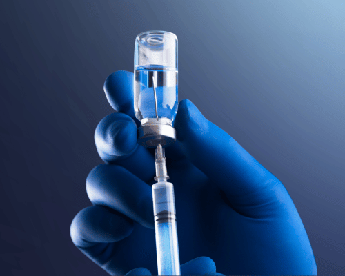 Photo of medical worker wearing blue glove holding vaccine and syringe