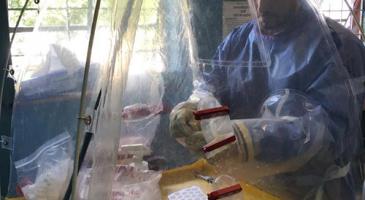 CDC biologist works on mobile biocontainment unit wearing protective gear