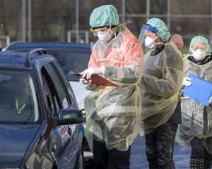 Photo of healthcare workers in protective gear talking to drivers in cars at a coronavirus drive-through testing site