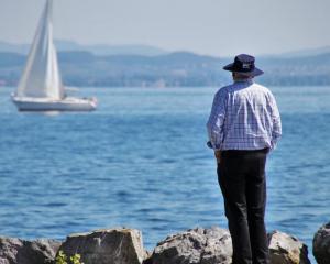Man standing on shore looking out at a sailboat on the water