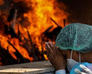 Masked woman prays before cremation site in India.